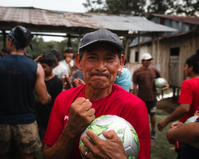 A village elder raising his fist in celebration while holding a new soccer ball