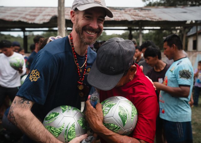 A team member embracing a community member, both holding new soccer balls