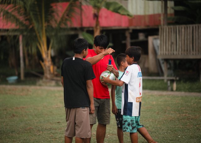 A volunteer inflating a new soccer ball for a group of boys