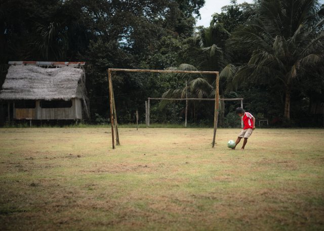 A boy kicking a ball alone in front of the goal