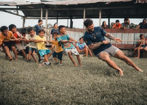 A team member and a line of children pulling together in a tug-of-war on a grass field